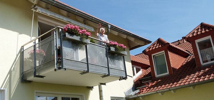 Eine Frau winkt vom Balkon ihrer Wohnung herunter