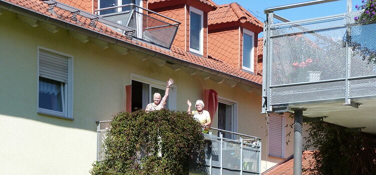 Bewohner winken vom Balkon ihrer Wohnung