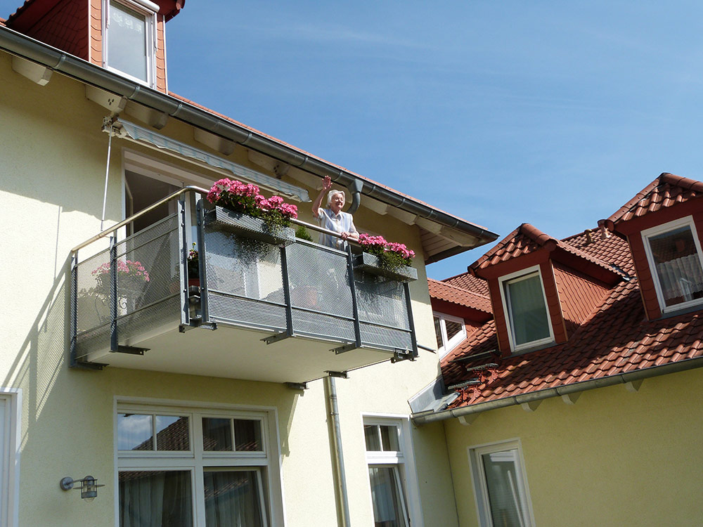 Eine Frau winkt vom Balkon ihrer Wohnung herunter