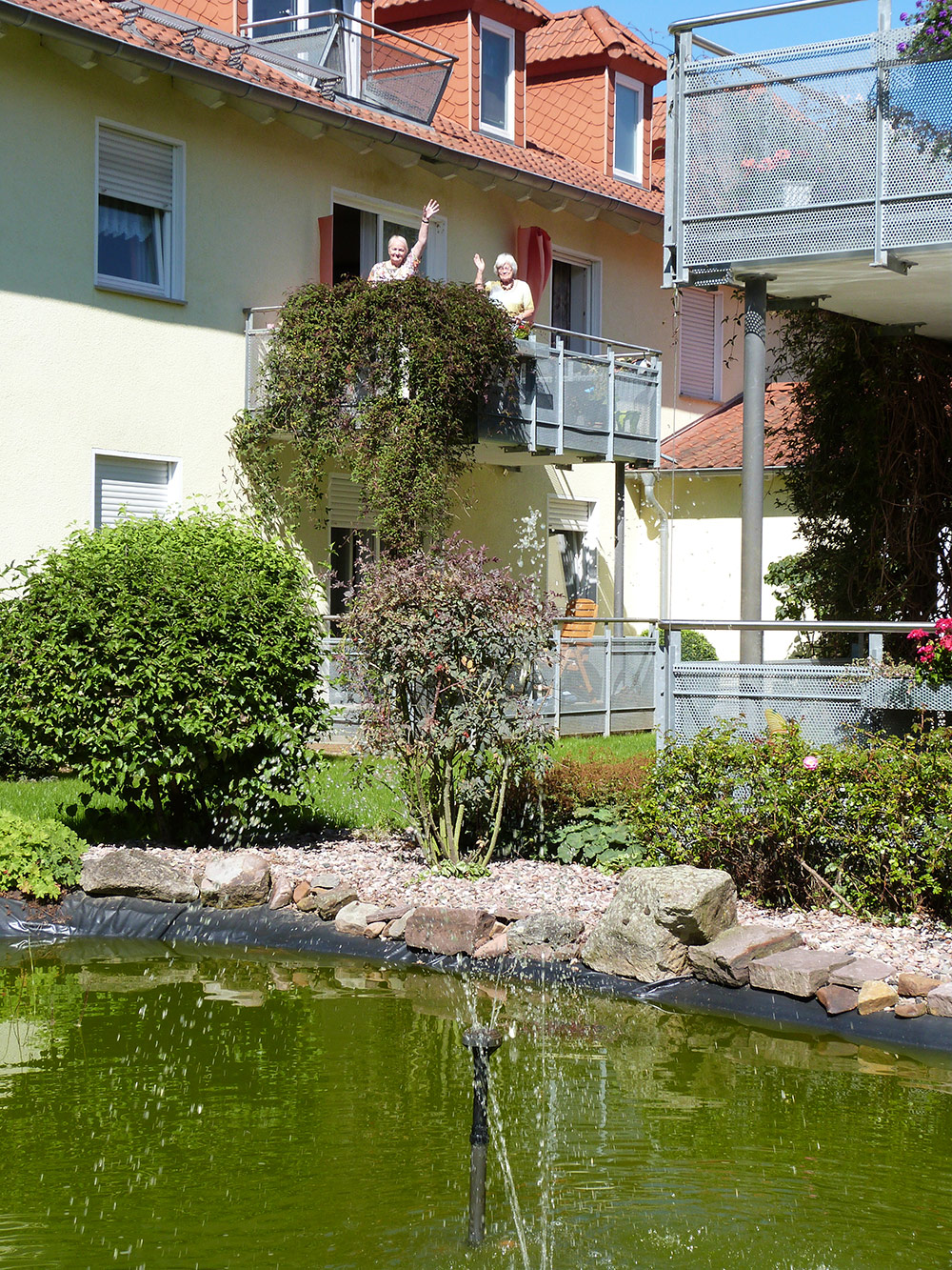 Bewohner winken vom Balkon ihrer Wohnung